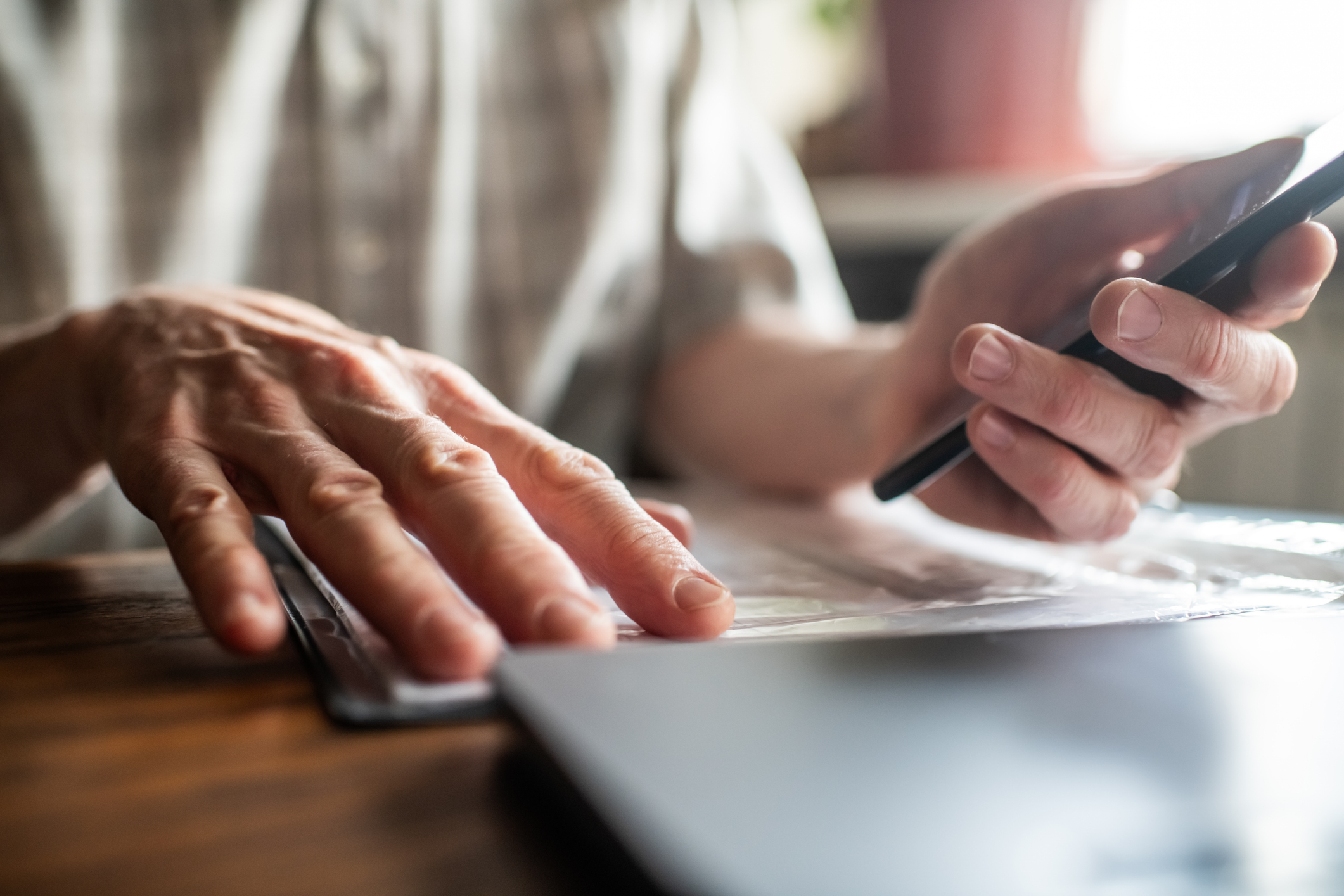 Senior man with smartphone examining bills, documents or receipts at home